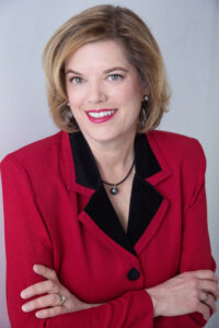 Dr. Faith Vilas looks at the camera. She wears a red blazer with a black collar. 
