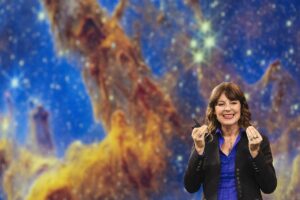 Dr. Lisa Kaltenegger wears a black blazer over a blue blouse in front of a Hubble Space Telescope image at TEDNext, October 22 - 24, 2024, Atlanta, GA. Photo: Erin Lubin / TED