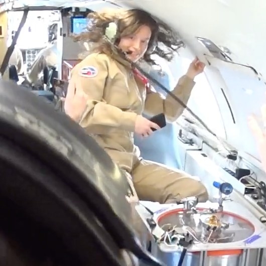 a white person in a beige flight suit floats in zero gravity